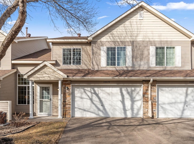 view of front of house with stone siding, driveway, a shingled roof, and a garage