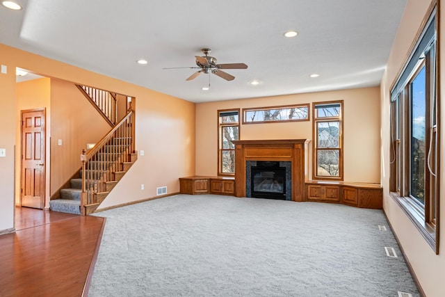 unfurnished living room featuring visible vents, recessed lighting, stairway, carpet floors, and a premium fireplace