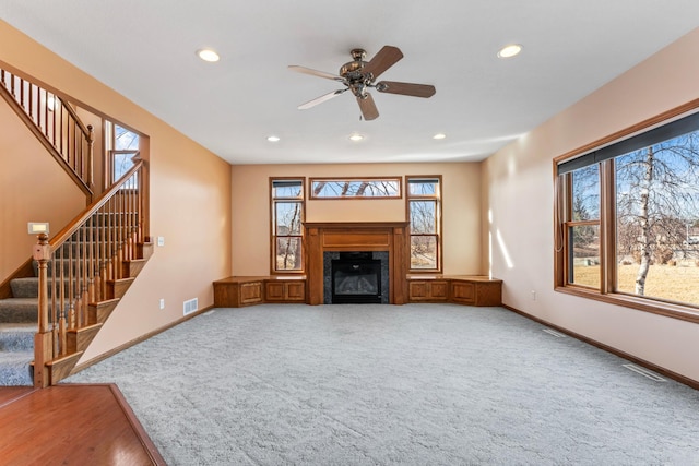 unfurnished living room featuring stairway, visible vents, baseboards, recessed lighting, and a glass covered fireplace