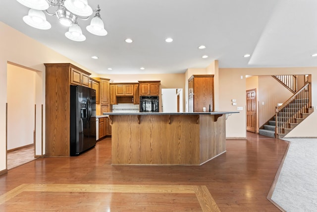 kitchen with brown cabinets, black appliances, a kitchen bar, and light wood-style floors