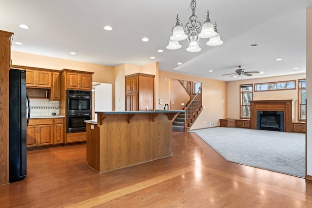 kitchen featuring wood finished floors, brown cabinetry, black appliances, a kitchen bar, and tasteful backsplash