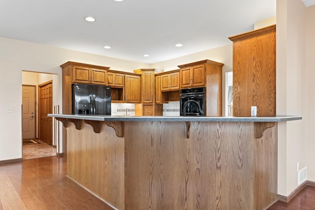 kitchen featuring black appliances, a kitchen breakfast bar, wood finished floors, and visible vents