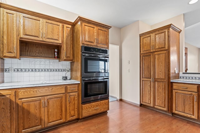 kitchen with light countertops, decorative backsplash, brown cabinets, light wood-style floors, and dobule oven black