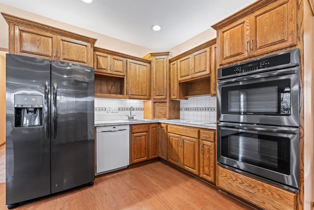 kitchen featuring multiple ovens, black fridge, a sink, light wood-style floors, and white dishwasher