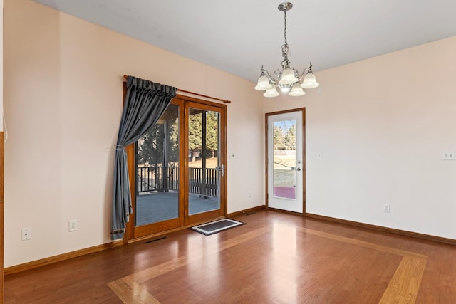 unfurnished room with a chandelier, baseboards, visible vents, and wood finished floors