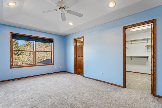 unfurnished bedroom with a raised ceiling, a spacious closet, carpet flooring, and baseboards