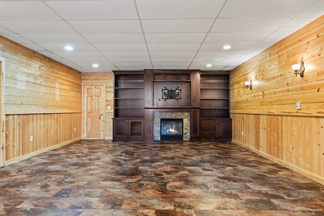 unfurnished living room featuring wooden walls, recessed lighting, baseboards, and a lit fireplace