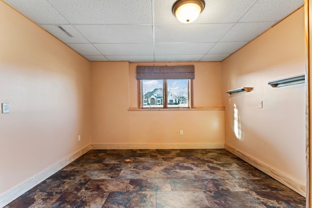 spare room featuring stone finish floor, a paneled ceiling, and baseboards