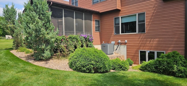 view of side of property with central air condition unit, a yard, and a sunroom