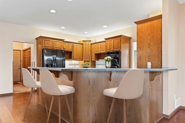 3135 Sherburn Pl SW, Rochester, MN 55902 - kitchen with black appliances, brown cabinetry, a breakfast bar area, wood finished floors, and recessed lighting