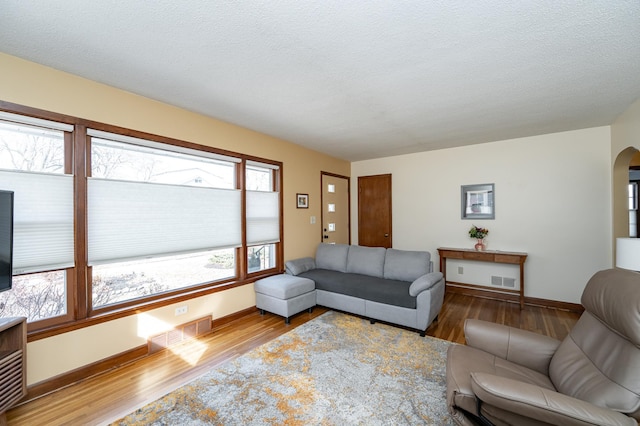 living area with visible vents, arched walkways, plenty of natural light, and wood finished floors