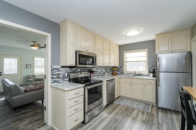 kitchen featuring a sink, cream cabinets, stainless steel appliances, light wood-style floors, and decorative backsplash