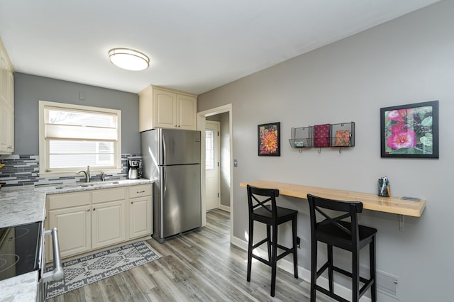 kitchen featuring light wood-style flooring, freestanding refrigerator, a sink, a kitchen breakfast bar, and backsplash