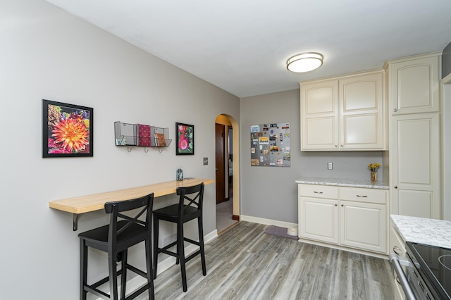 kitchen featuring baseboards, arched walkways, cream cabinets, and light wood-style flooring