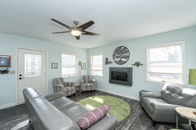 living room with a glass covered fireplace, dark wood-type flooring, a healthy amount of sunlight, and baseboards