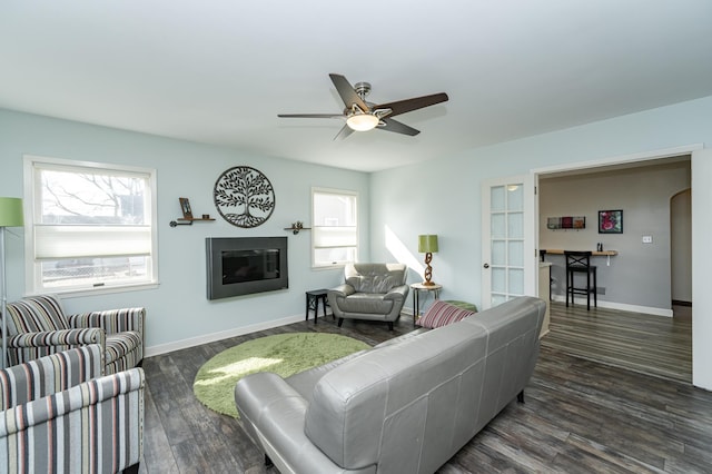 living room featuring arched walkways, a glass covered fireplace, dark wood finished floors, and a wealth of natural light