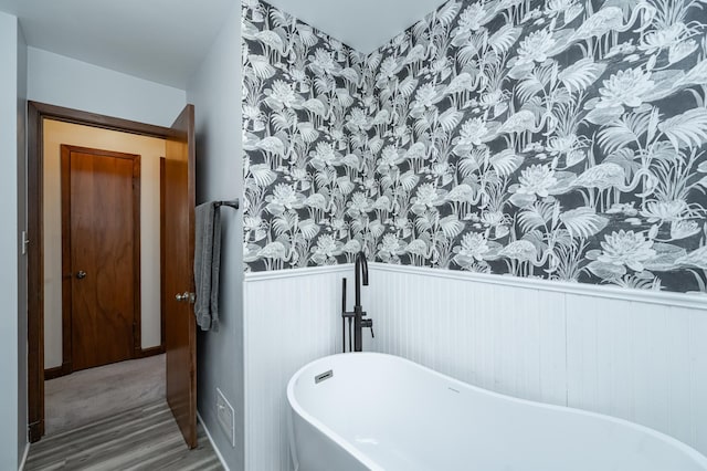 bathroom with a freestanding bath, wood finished floors, and wainscoting