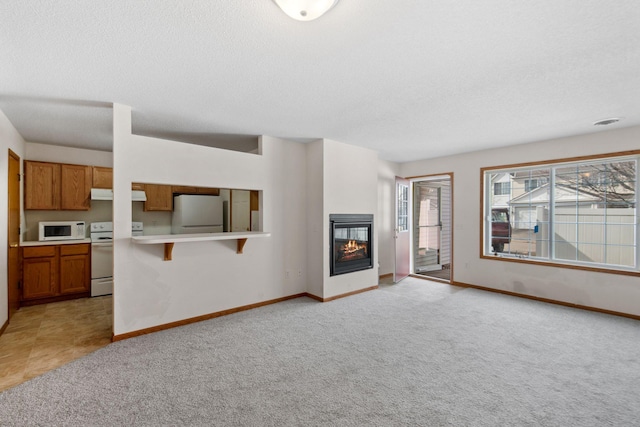 unfurnished living room featuring a glass covered fireplace, light colored carpet, a textured ceiling, and baseboards