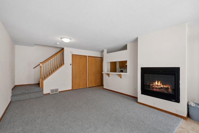 unfurnished living room featuring a glass covered fireplace, stairway, baseboards, and visible vents