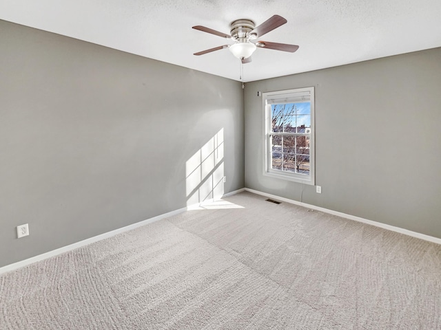 empty room with carpet, visible vents, baseboards, ceiling fan, and a textured ceiling