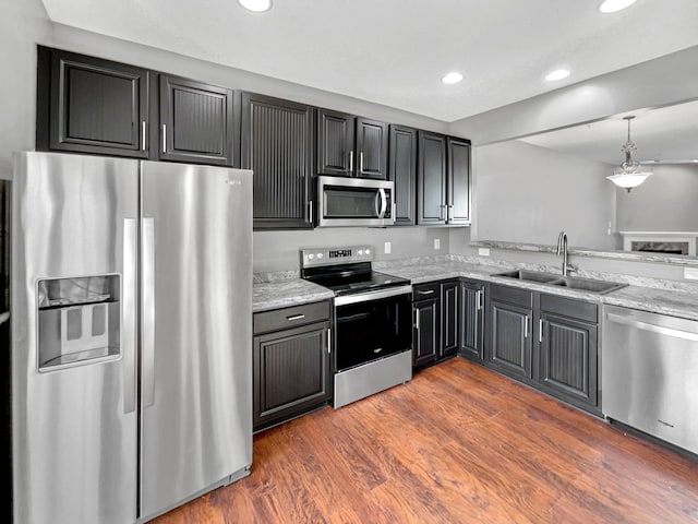 kitchen with a sink, light stone countertops, recessed lighting, appliances with stainless steel finishes, and dark wood-style flooring