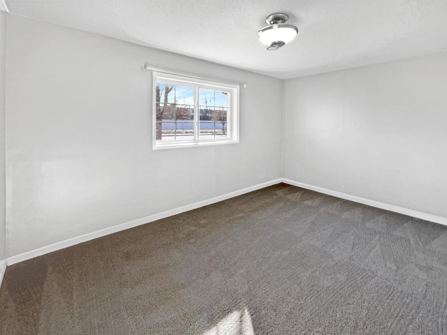 empty room with baseboards, dark carpet, and a textured ceiling