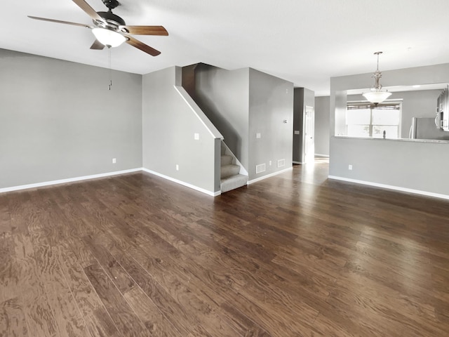 unfurnished living room with ceiling fan, baseboards, dark wood-style floors, and stairs