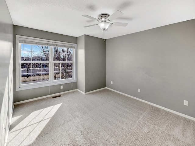 carpeted spare room with a ceiling fan, baseboards, and a textured ceiling