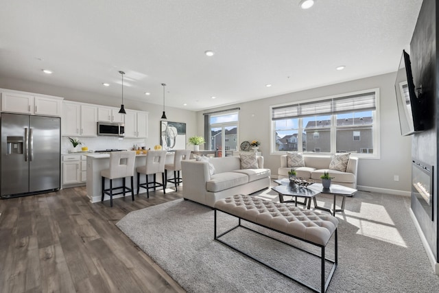 living area with a glass covered fireplace, dark wood-type flooring, recessed lighting, and baseboards