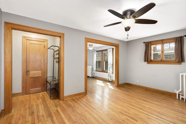 spare room featuring a ceiling fan, radiator heating unit, and light wood finished floors