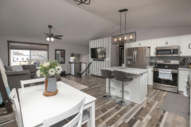 kitchen with a kitchen island, lofted ceiling, appliances with stainless steel finishes, white cabinetry, and open floor plan