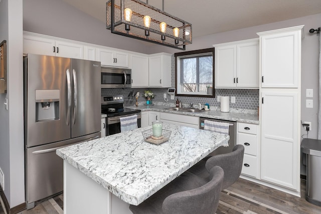 kitchen featuring backsplash, a breakfast bar, appliances with stainless steel finishes, wood finished floors, and white cabinets