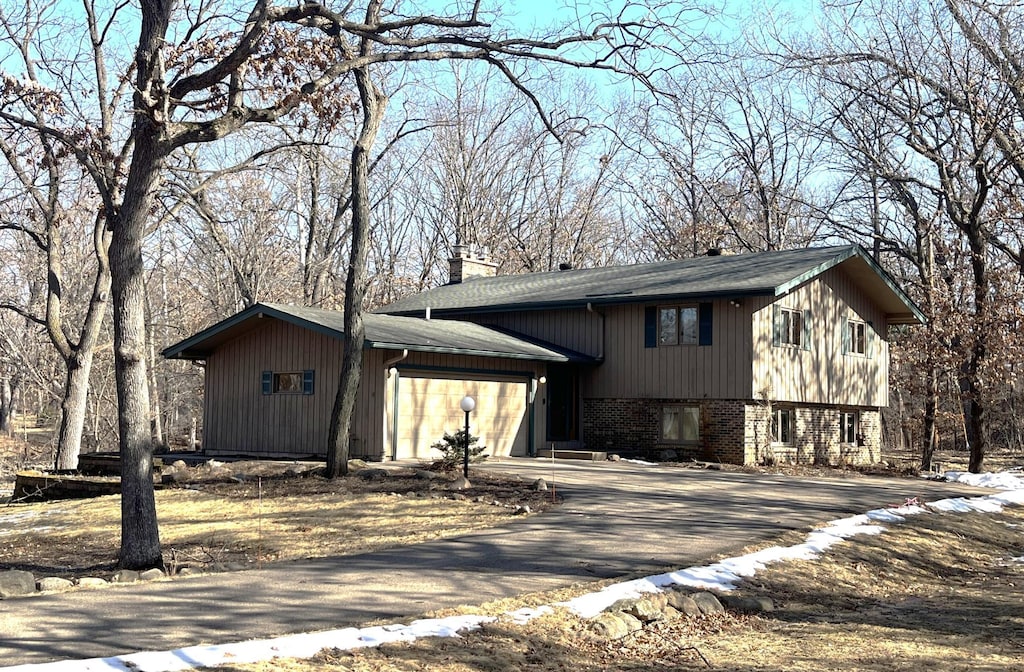 tri-level home featuring a garage, driveway, brick siding, and a chimney