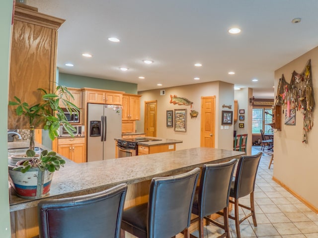 kitchen featuring a kitchen bar, recessed lighting, stainless steel appliances, a peninsula, and light tile patterned flooring