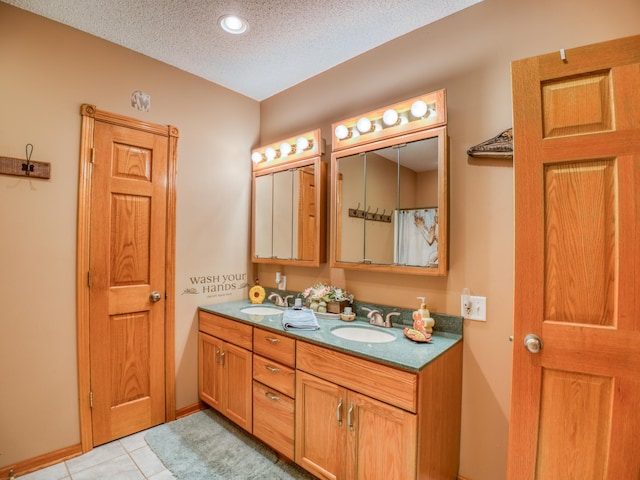 bathroom featuring tile patterned floors, a sink, a textured ceiling, double vanity, and baseboards