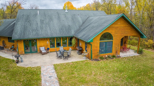 rear view of house with a patio, a lawn, and roof with shingles