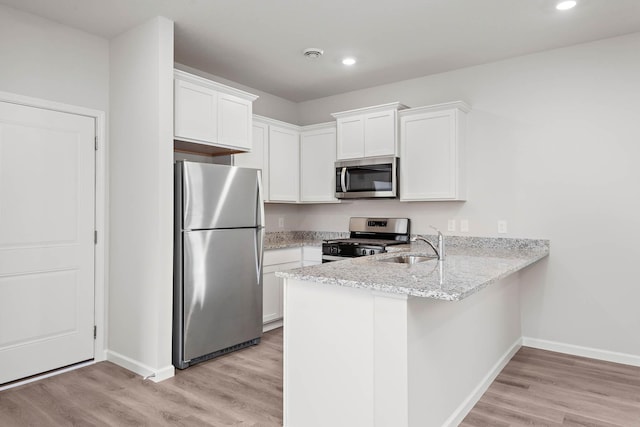 kitchen with appliances with stainless steel finishes, a peninsula, white cabinets, light wood finished floors, and light stone countertops