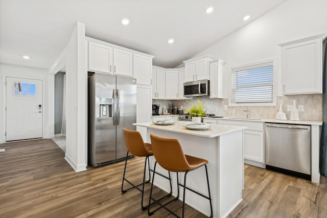 kitchen with a breakfast bar, a sink, stainless steel appliances, white cabinetry, and a center island