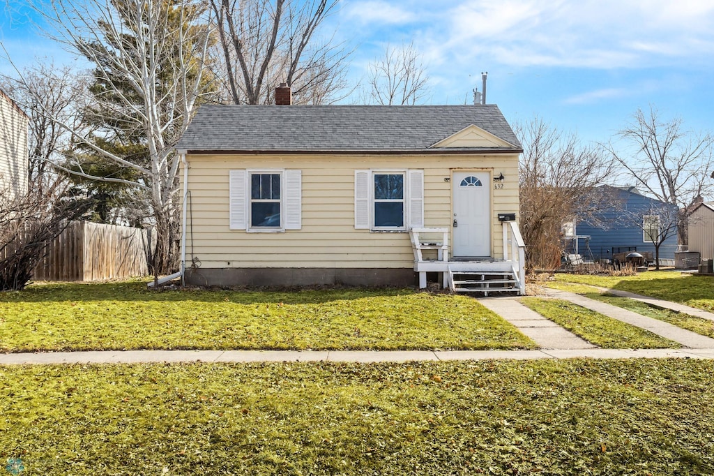 bungalow with roof with shingles, a chimney, a front yard, and fence