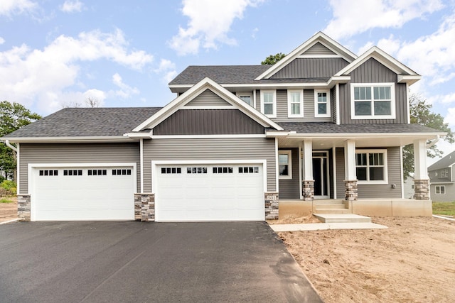 craftsman house featuring driveway, roof with shingles, an attached garage, covered porch, and stone siding