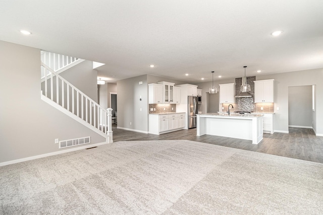 unfurnished living room featuring visible vents, baseboards, recessed lighting, a sink, and stairs