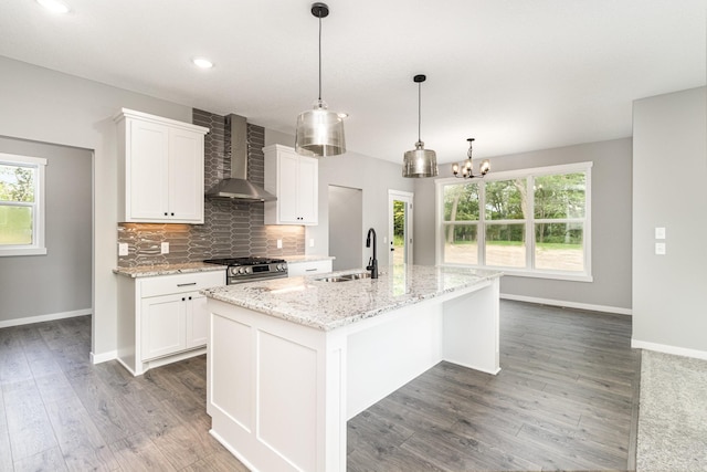 kitchen with gas stove, a sink, white cabinetry, wall chimney exhaust hood, and backsplash