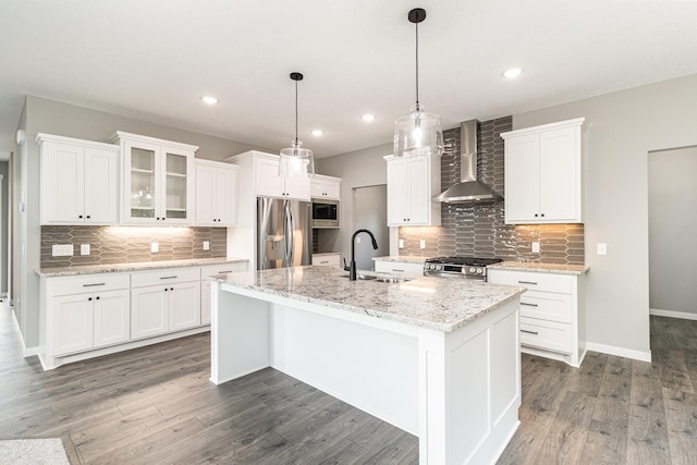 kitchen with a center island with sink, wood finished floors, stainless steel appliances, wall chimney exhaust hood, and a sink