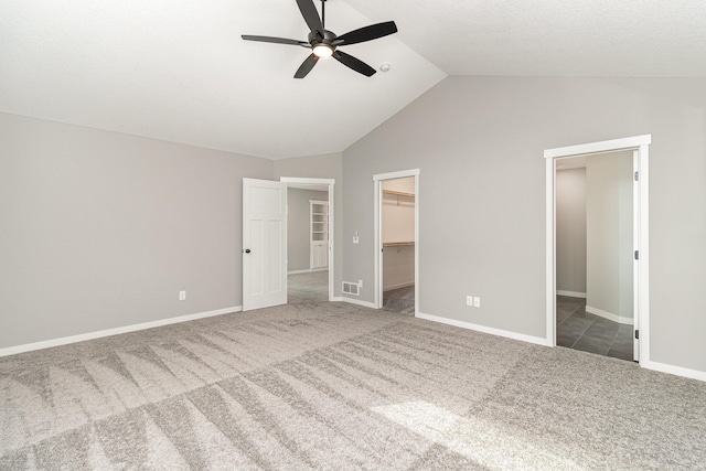 unfurnished bedroom with a walk in closet, baseboards, carpet flooring, and vaulted ceiling