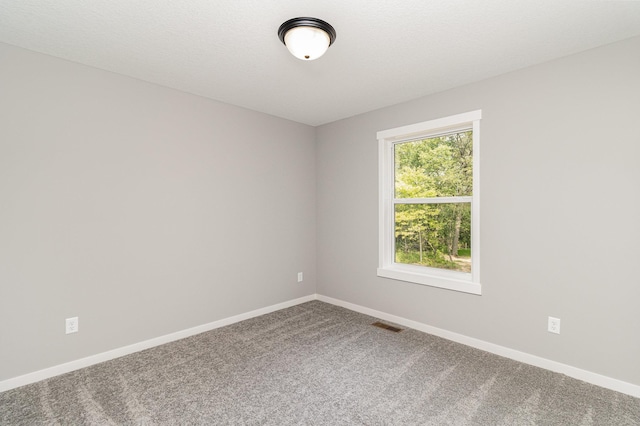 empty room featuring carpet flooring, visible vents, a textured ceiling, and baseboards