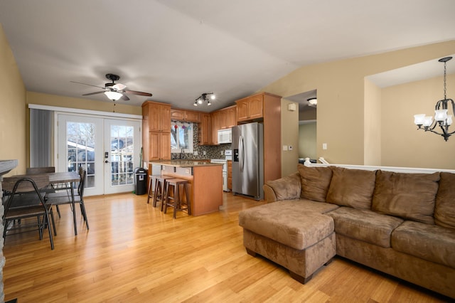 living room with ceiling fan with notable chandelier, french doors, light wood-type flooring, and lofted ceiling