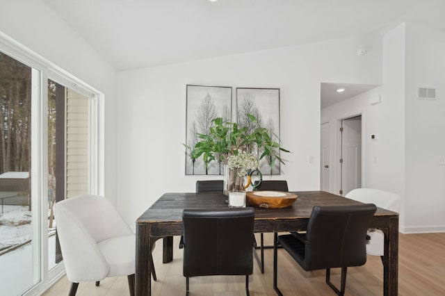 dining space with light wood finished floors, visible vents, a healthy amount of sunlight, and vaulted ceiling