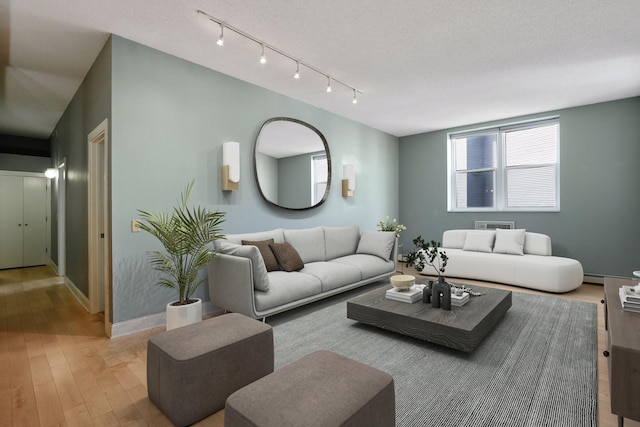 living room with rail lighting, a textured ceiling, light wood-type flooring, and baseboards