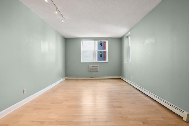 unfurnished room with a textured ceiling, a baseboard radiator, light wood-style floors, and a wall unit AC