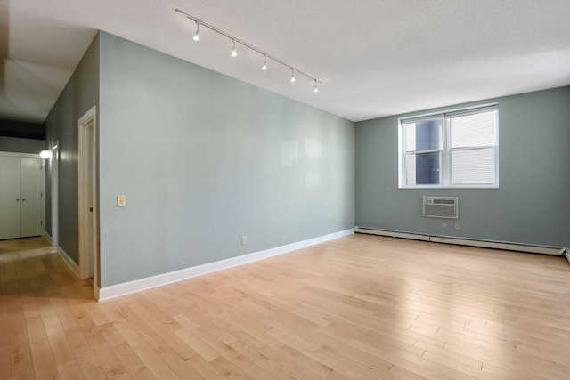 spare room featuring baseboards, an AC wall unit, light wood-style floors, a textured ceiling, and a baseboard heating unit